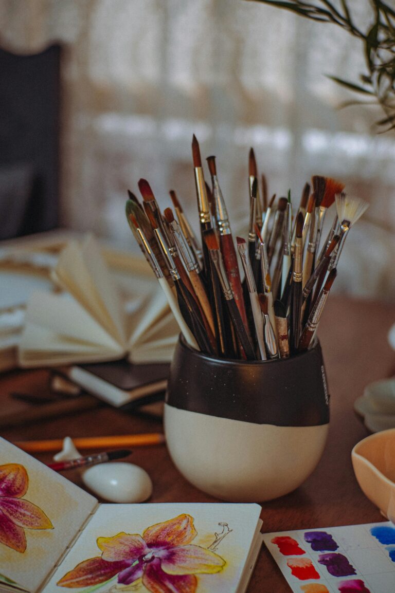 Cozy artistic workspace featuring a collection of paintbrushes, sketchbooks, and watercolor palettes.